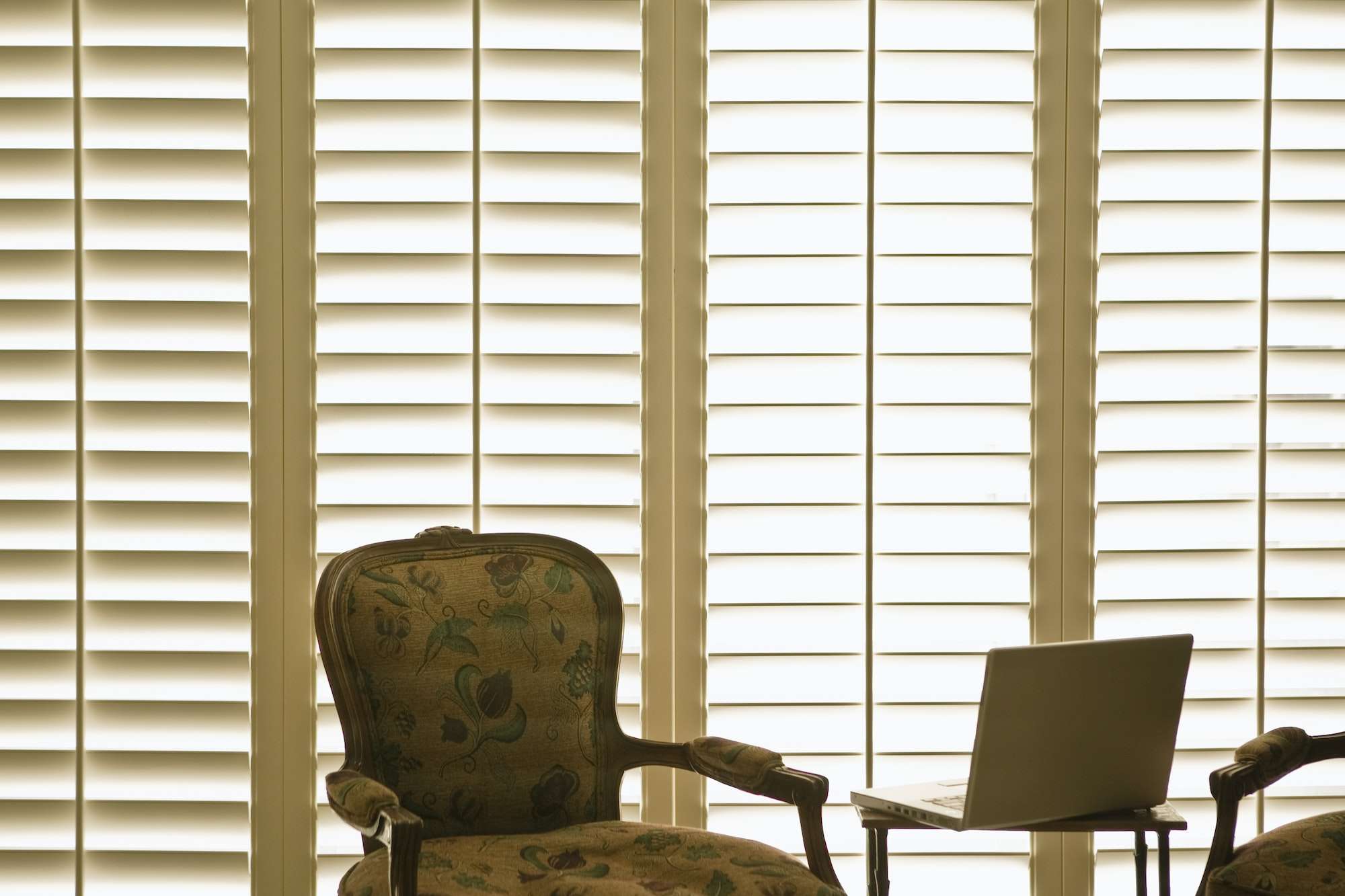 A chair and table in front of two windows.