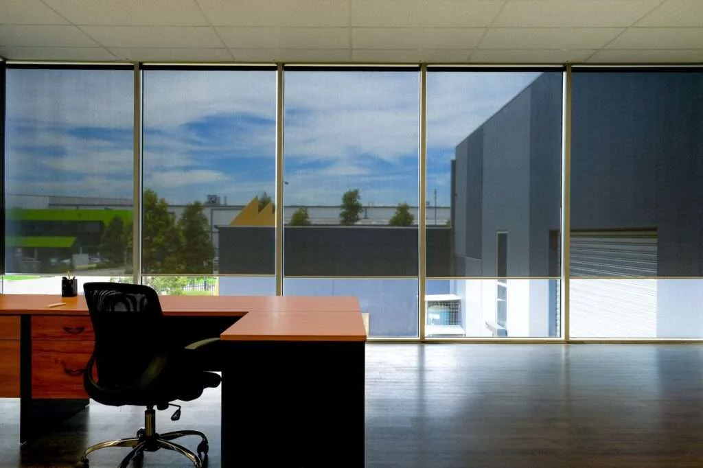 A desk and chair in front of large windows.