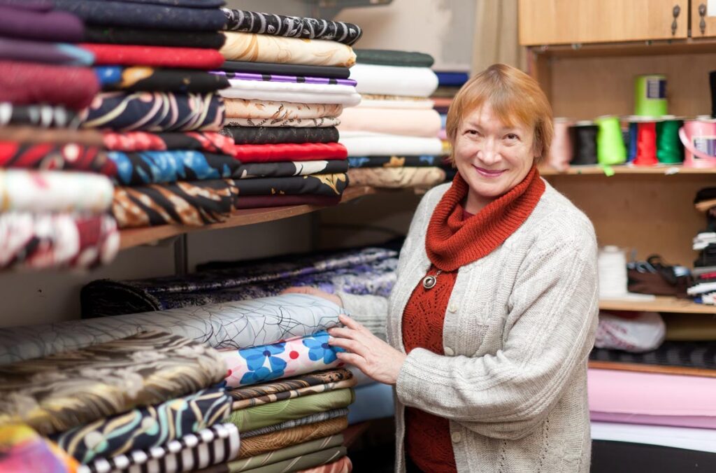 A woman standing in front of a shelf filled with fabric.